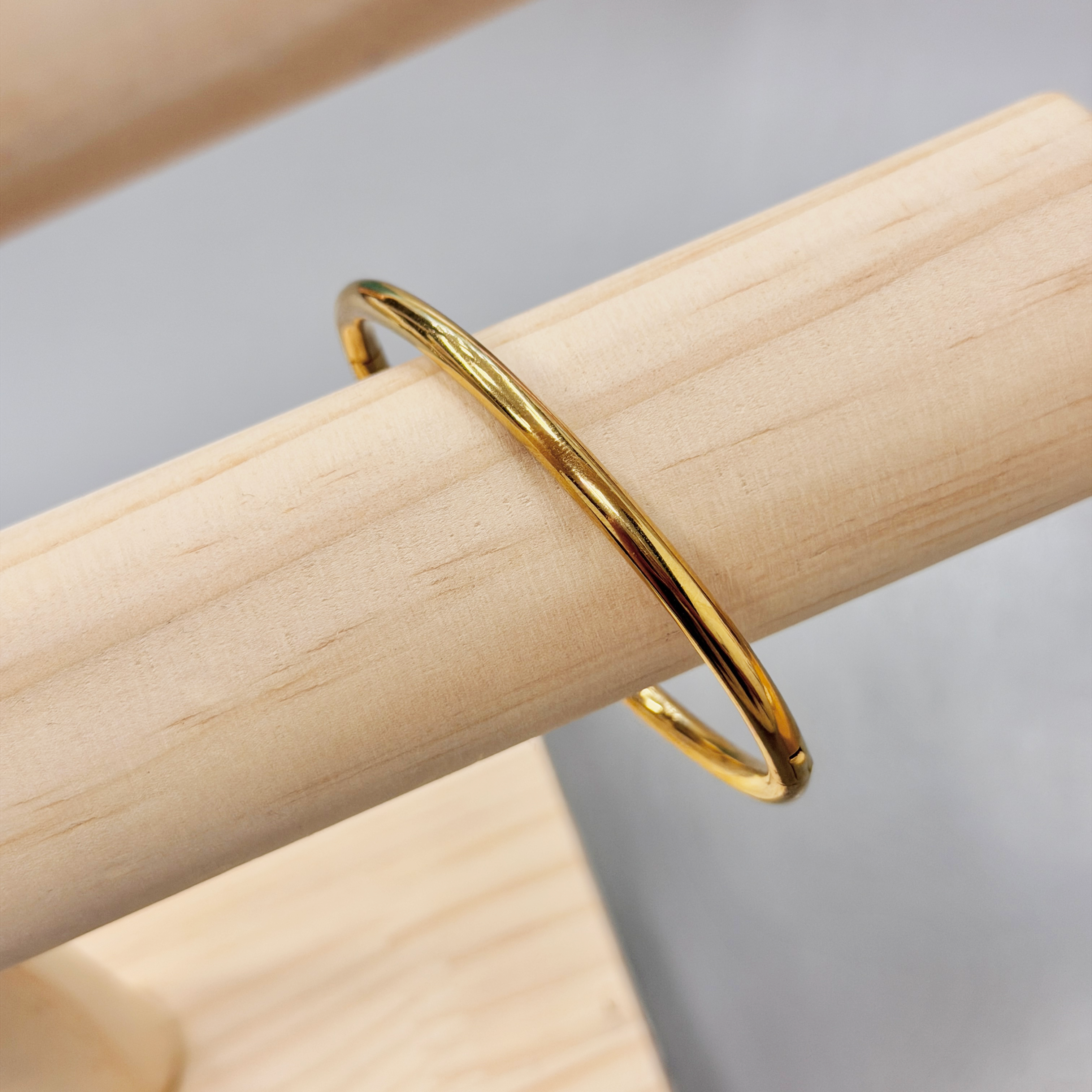 Close-up of a gold metal ring resting on a light wooden plank, photographed at a diagonal angle.