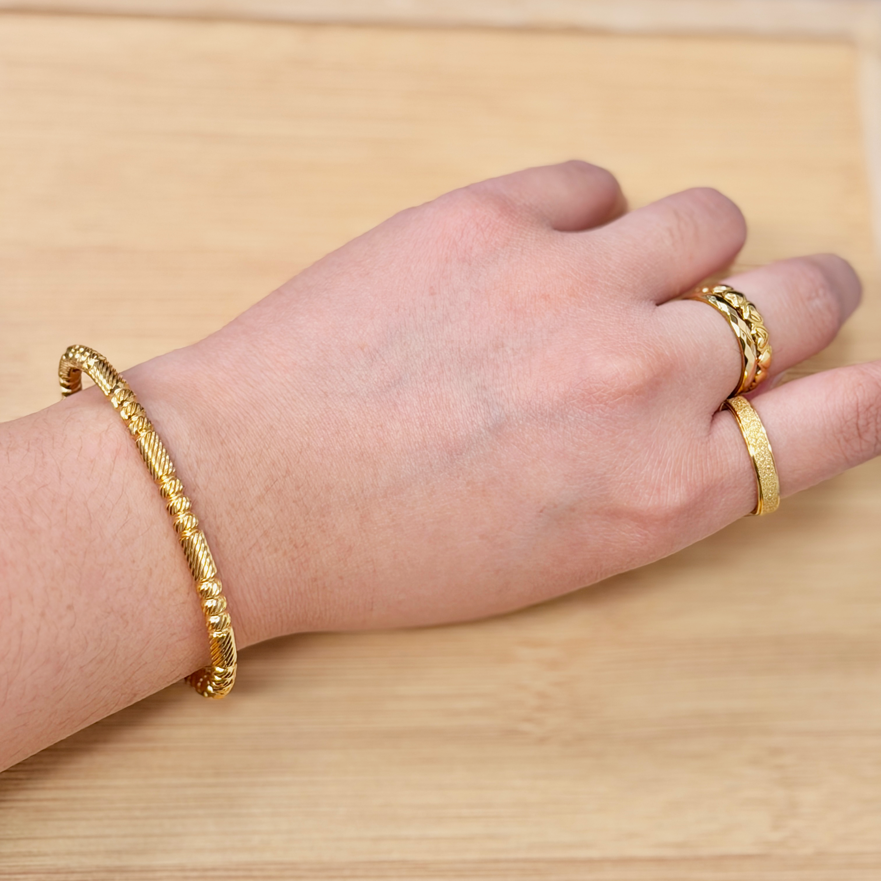 Close-up of a person's wrist wearing a gold bracelet and ring, resting on a light wooden surface.