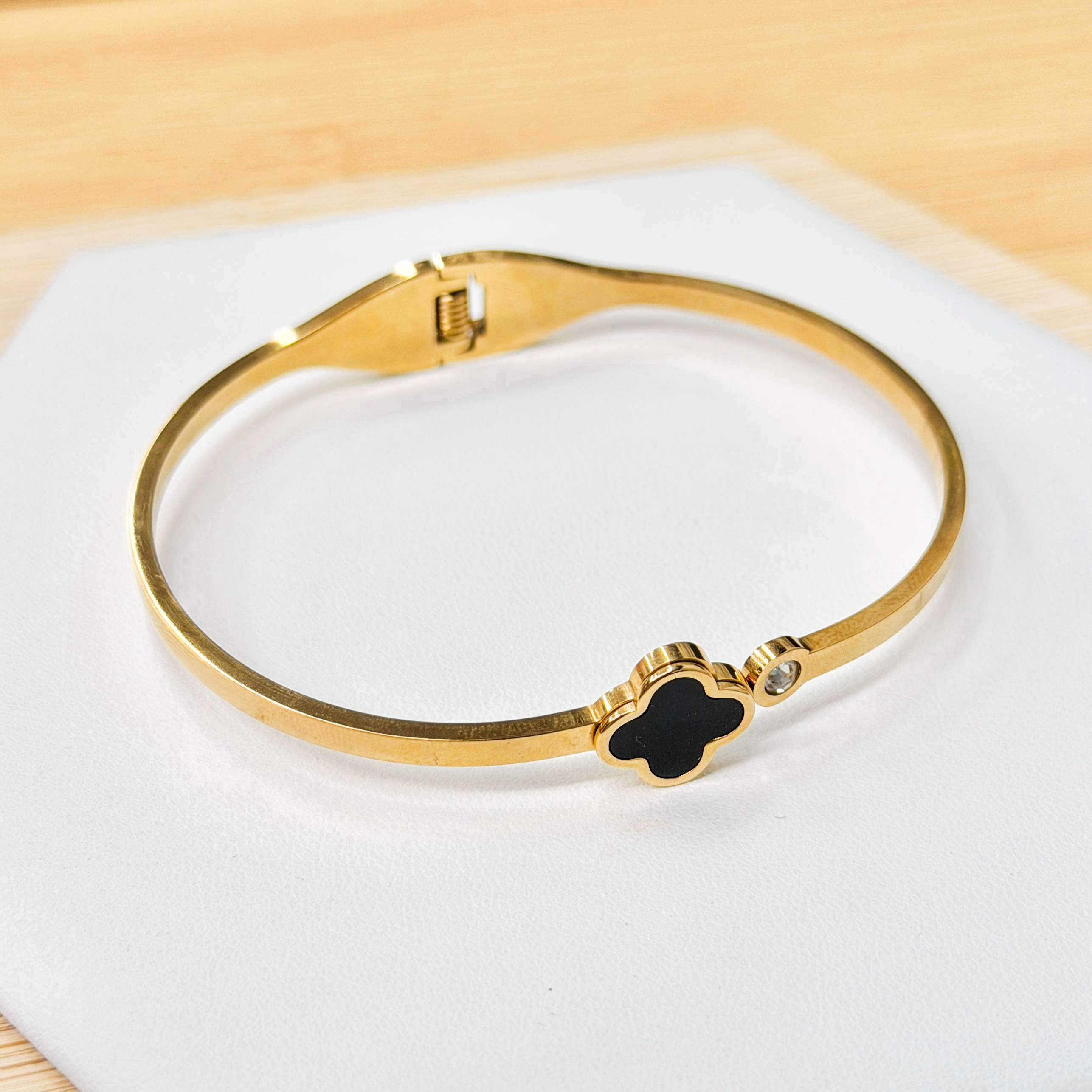 Gold-toned bracelet with a black clover-shaped centerpiece resting on a white display surface.