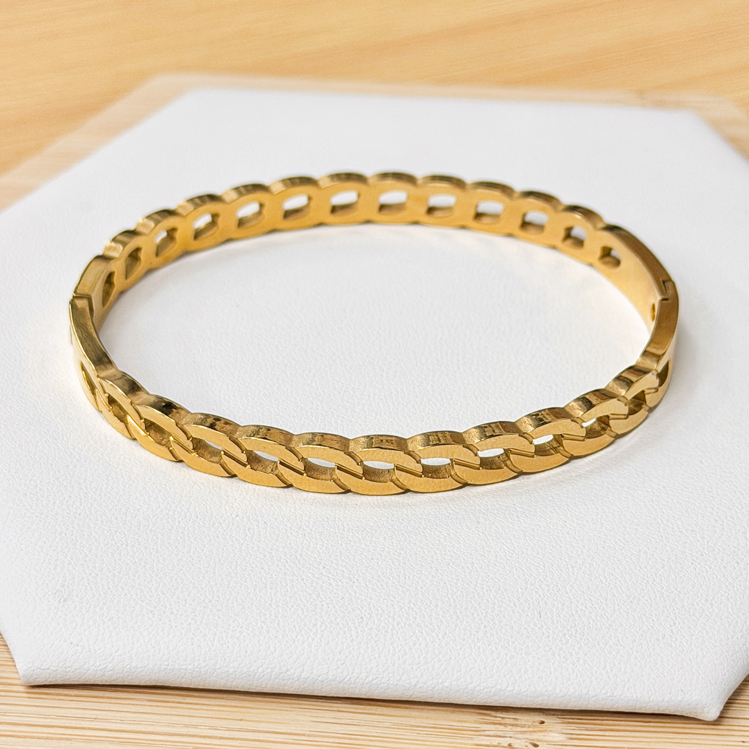 Gold-tone link bracelet curved on a white display pad placed on a light wooden surface.