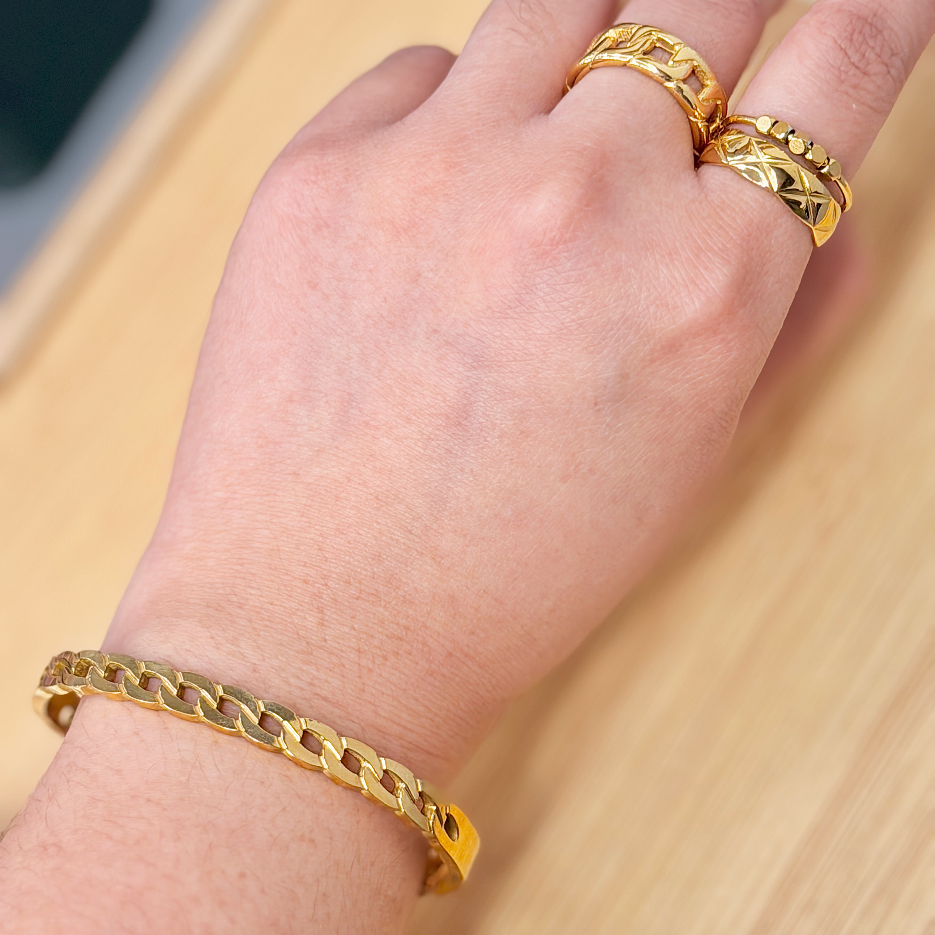 Close-up of a wrist wearing a gold chain bracelet with circular links on a light background.