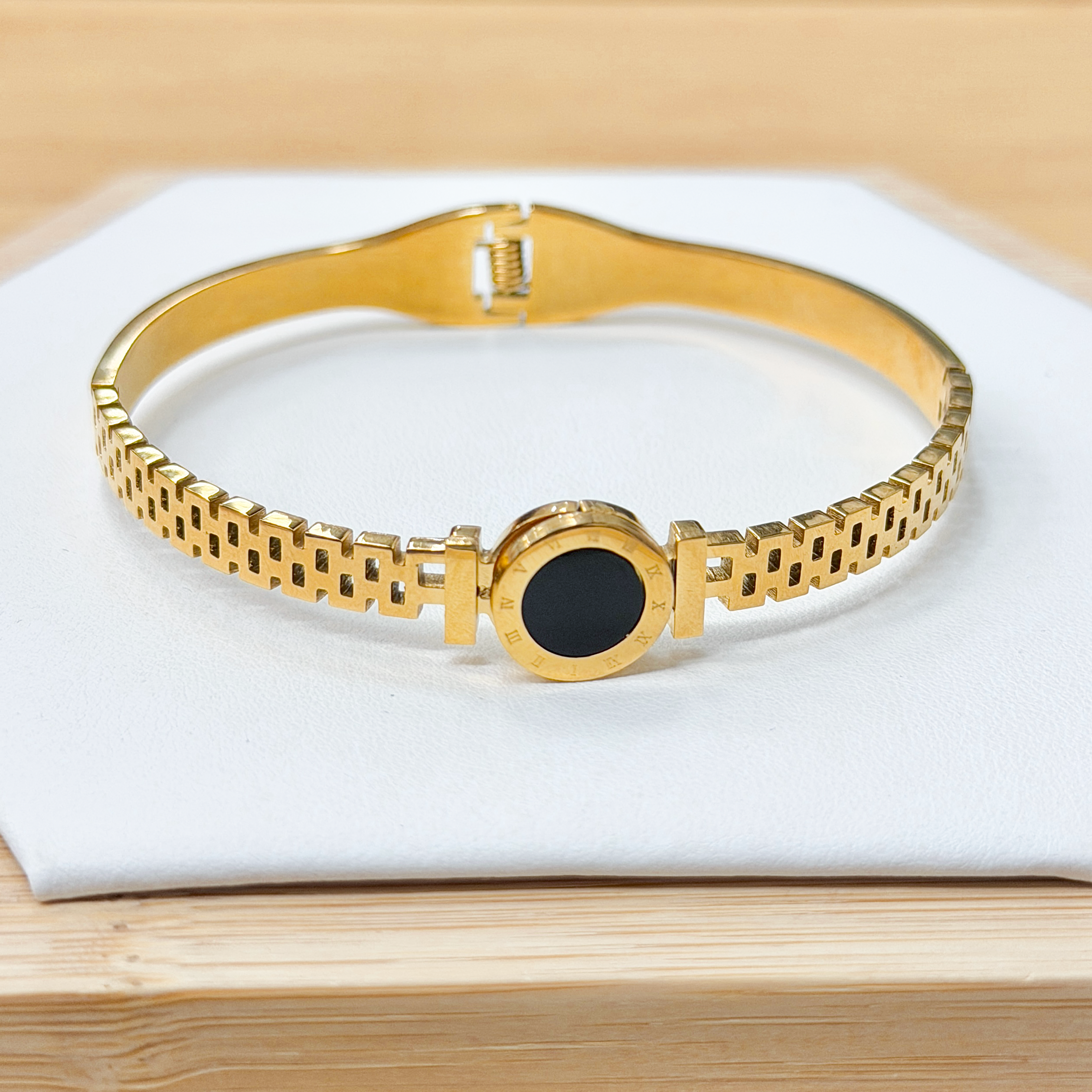 Watch Band Roman Numeral Black Inlay Link Bangle picture2 - Eriy Gift Gold bracelet with a black circular centerpiece resting on a white cushion in a wooden display box.