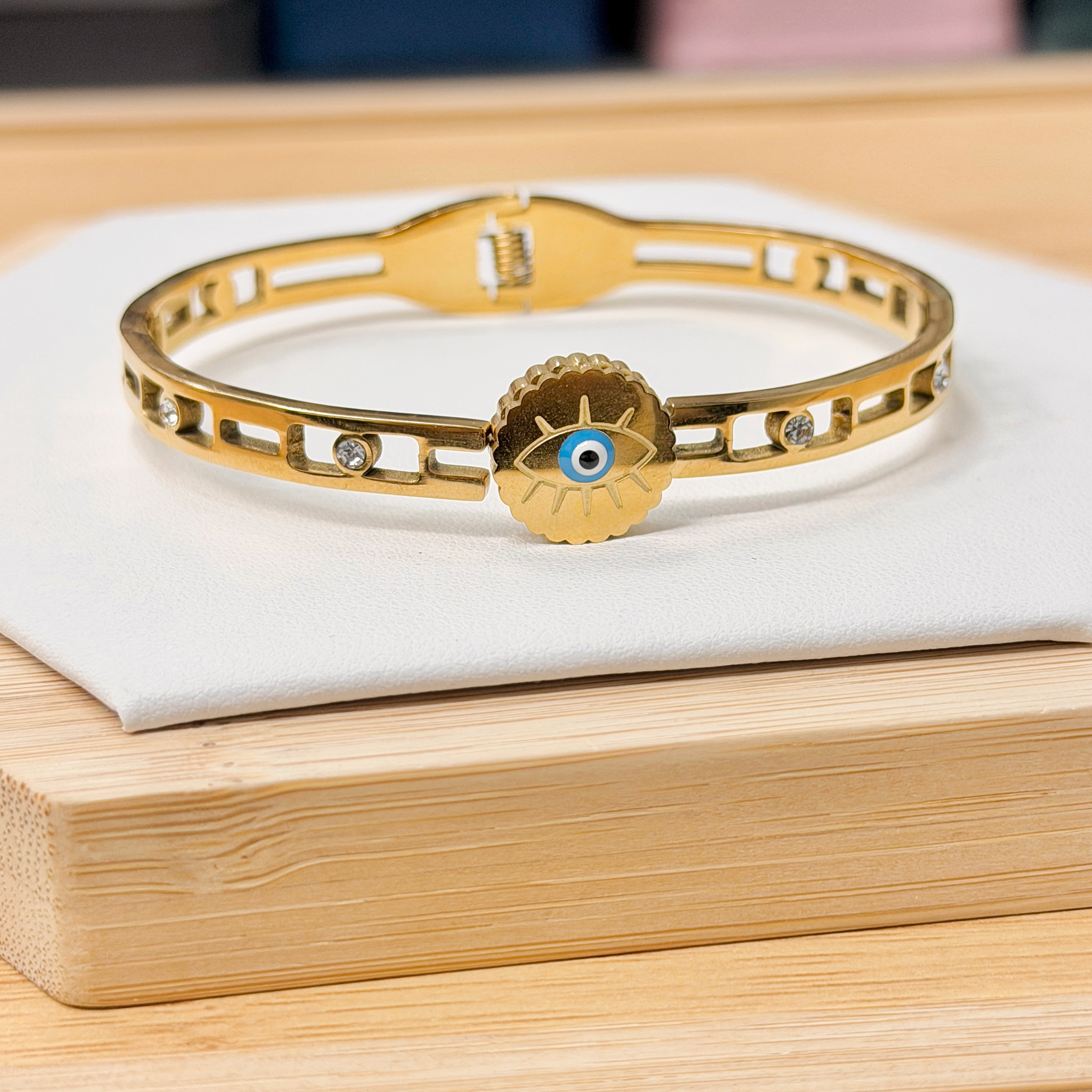 Zircon Inlaid Hollow Band Evil Eye Gold Bangle picture2 - Eriy Gift Gold bracelet with a blue-eyed charm resting on a white surface.