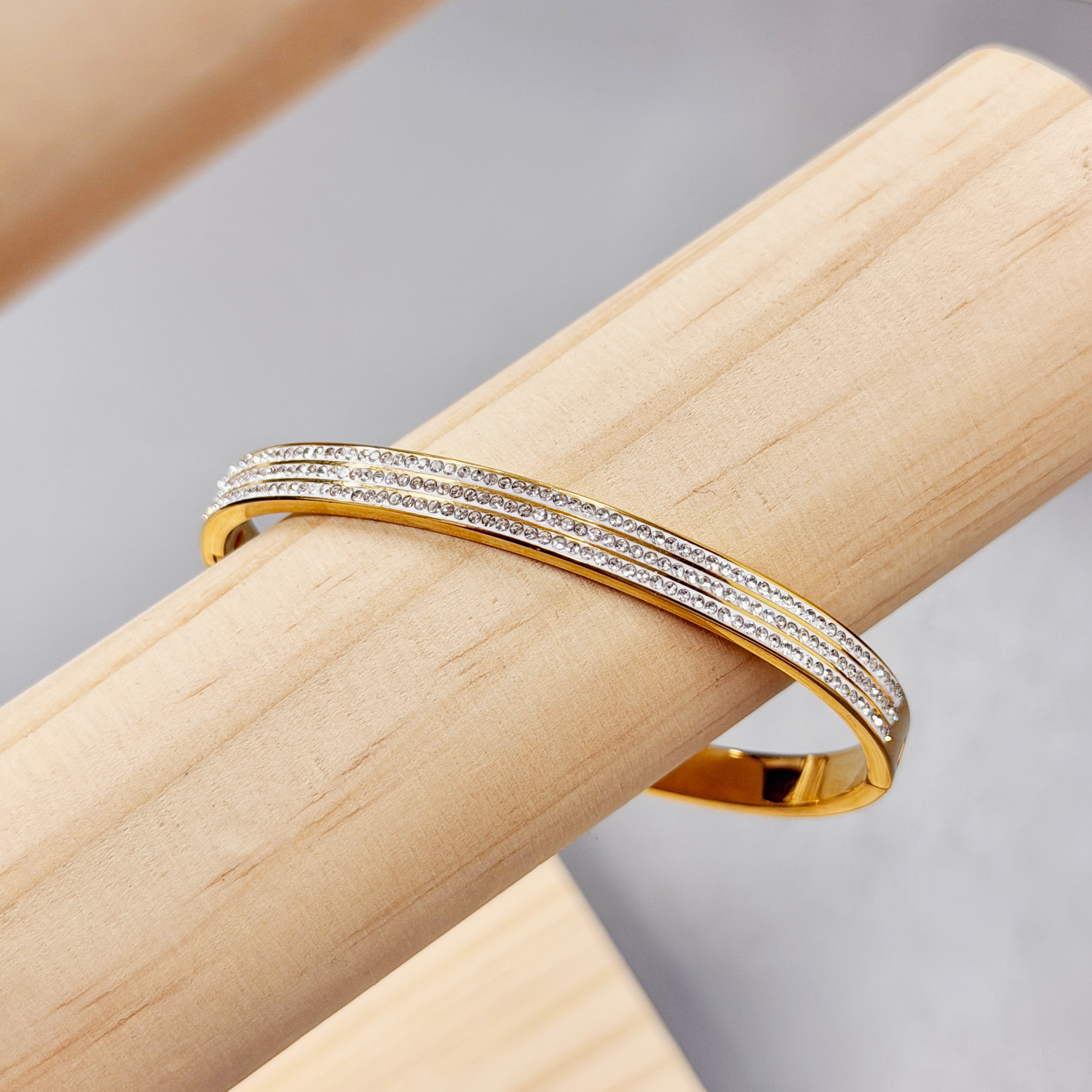 Zircon Paved Triple line Gold Bangle picture3 - Eriy Gift Diamond-studded gold bracelet curved on a light wood surface.